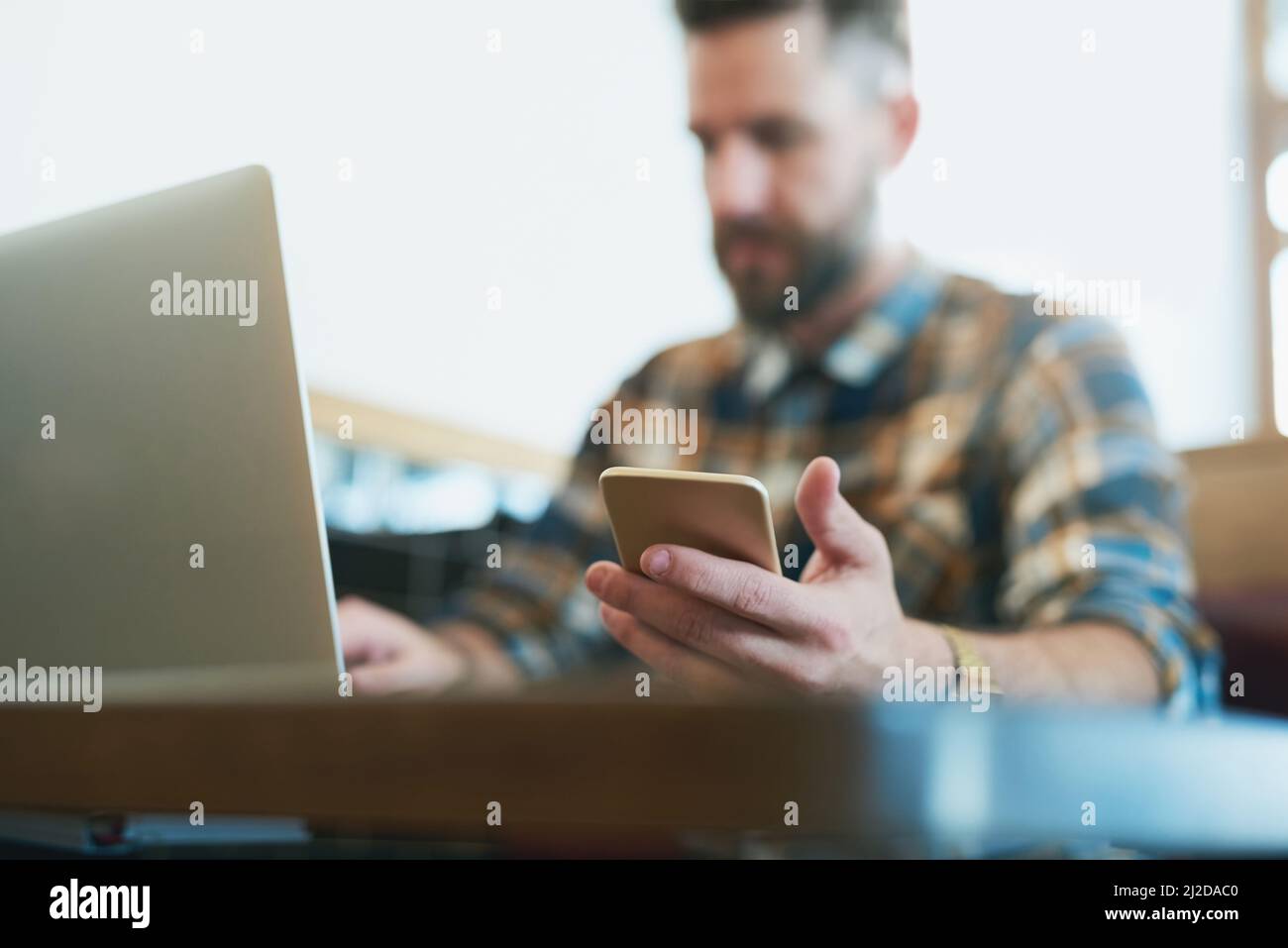 Take your wireless devices wherever you go. Shot of a young man using his cellphone and laptop while sitting in a cafe. Stock Photo