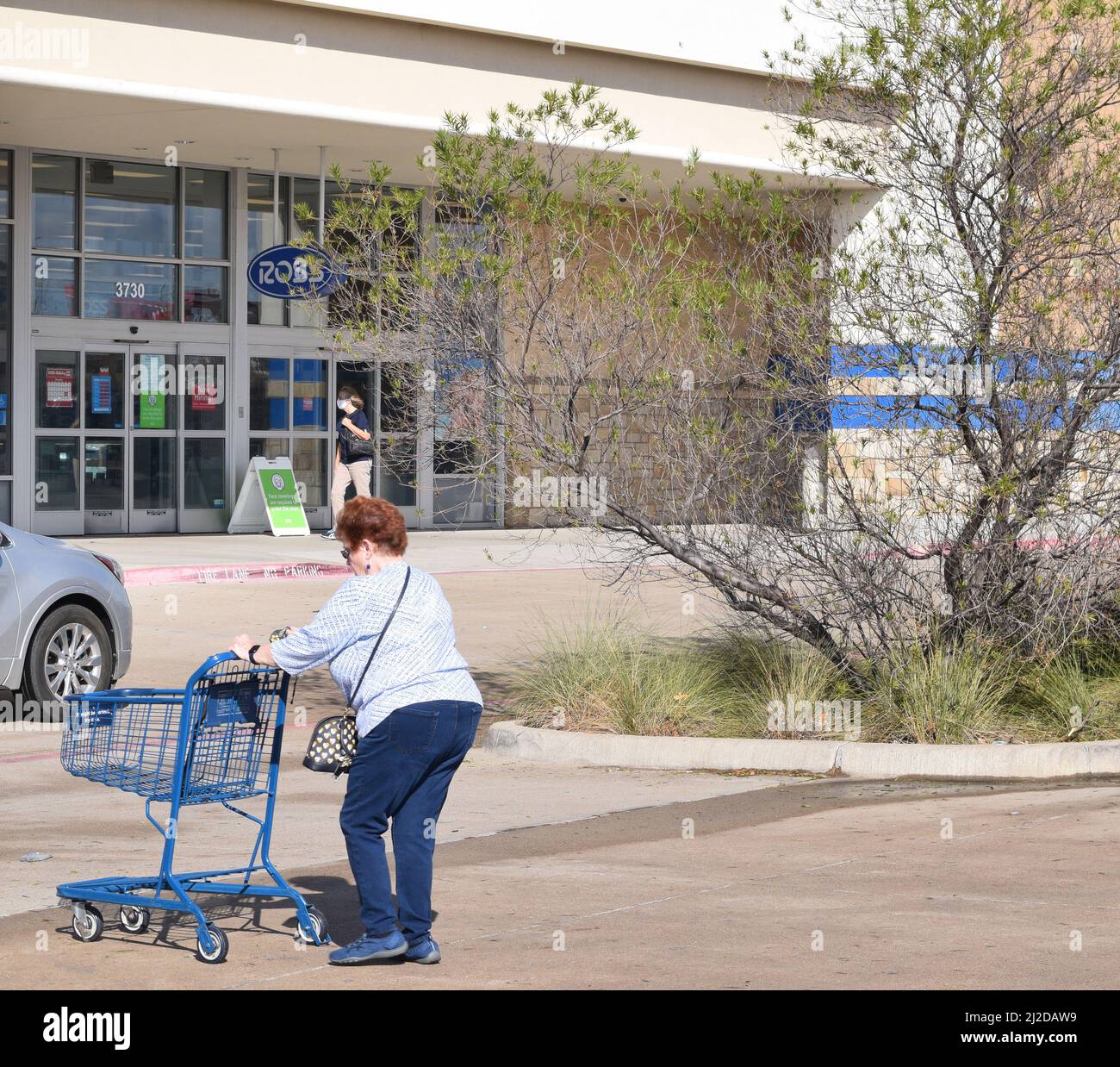 Woman pushes a shopping cart toward a Ross Dress for Less store Stock Photo