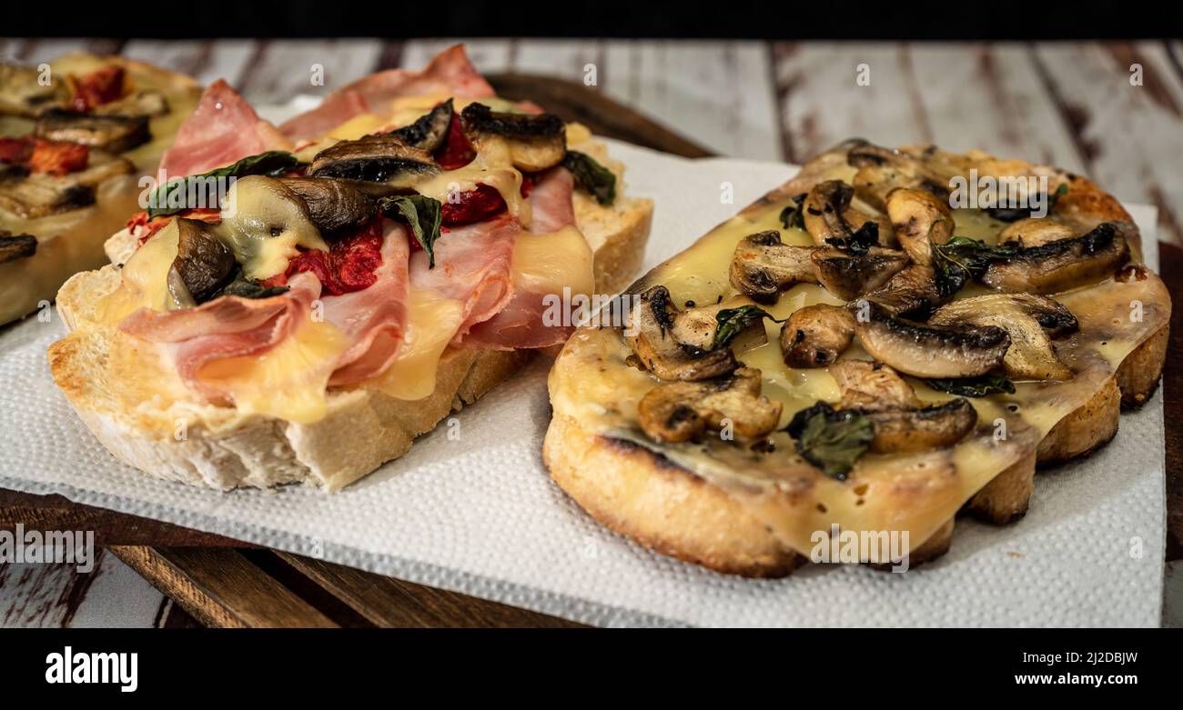 Large bruschettas with cheese, mushrooms, prosciutto and tomato in different combinations. Mediterranean food concept. Stock Photo