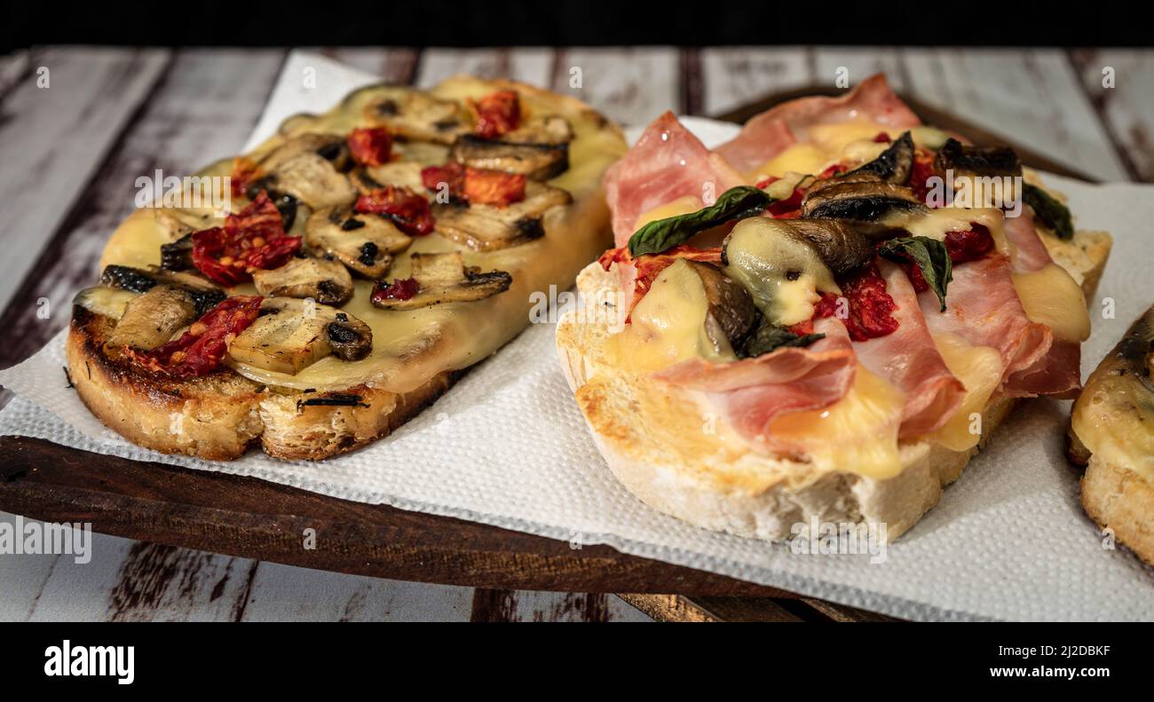 Large bruschettas with cheese, mushrooms, prosciutto and tomato in different combinations. Mediterranean food concept. Stock Photo
