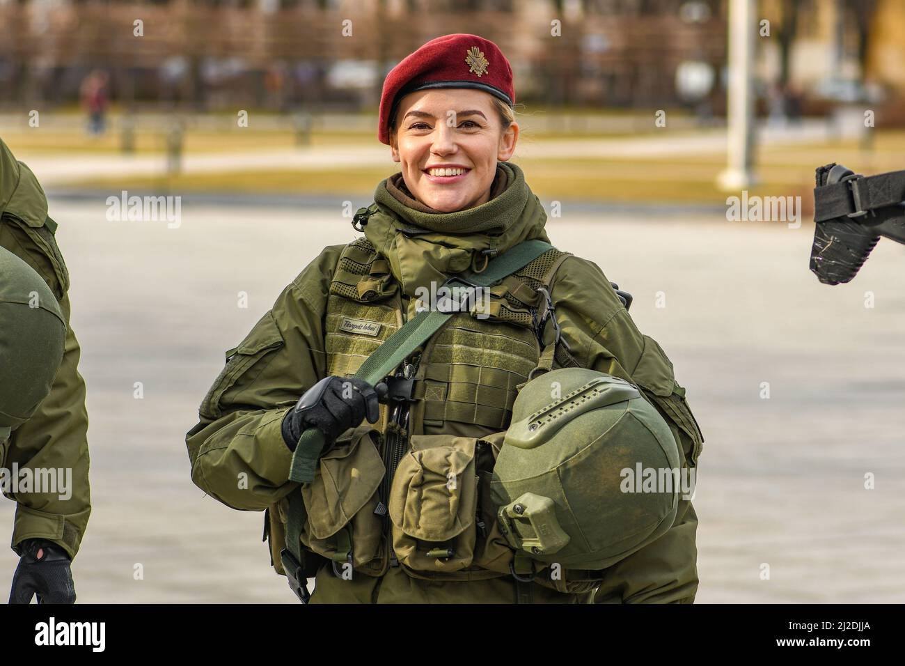 Beautiful smiling blonde hair girl member of Lithuanian Armed Forces with weapons in the city, NATO force integration unit Stock Photo