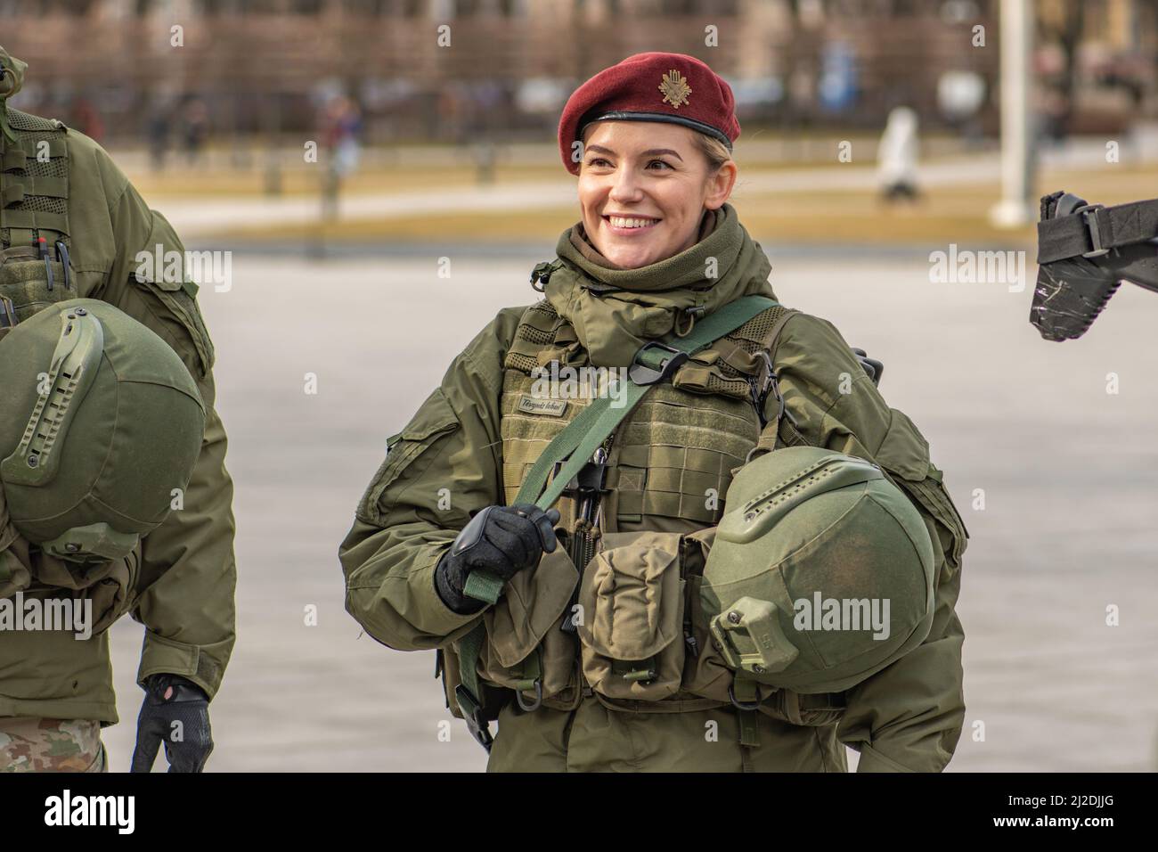 Beautiful smiling blonde hair girl member of Lithuanian Armed Forces with weapons in the city, NATO force integration unit Stock Photo