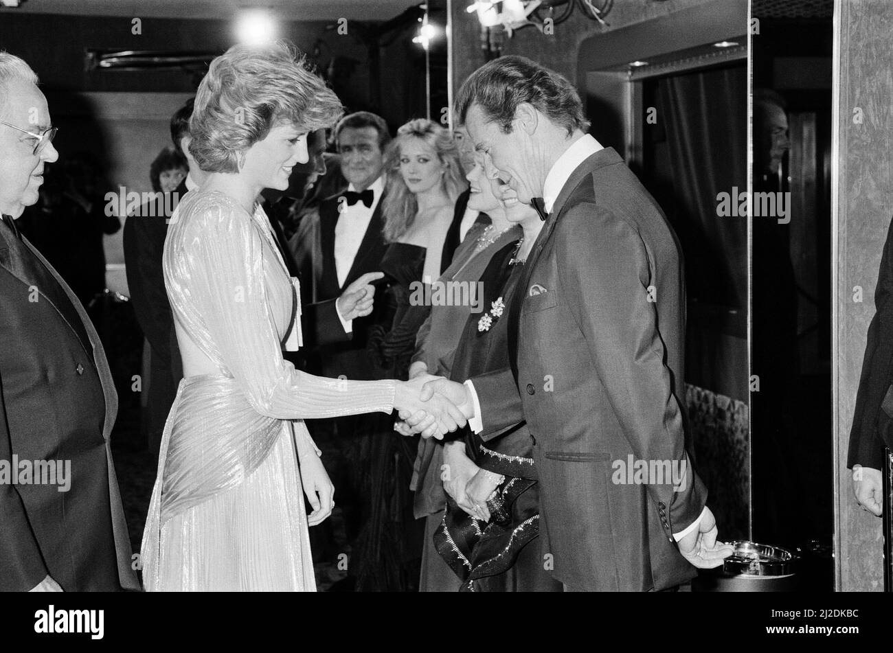 HRH The Princess of Wales, Princess Diana greets lead actor Roger Moore at The Royal Premiere of the 14th 007 James Bond Movie, 'A View To A Kill'  at the Odeon Cinema, Leicester Square, London. Roger bows and they shake hands.  This was Roger Moore's last of seven Bond Films. His first 'Live and Let Die', was released in 1973.  Princess Diana wears a stunning silver Bruce Oldfield dress.   In the background is actor Patrick Macnee, who plays Sir Godfrey Tibbett in the film.  Picture taken 14th June 1985 Stock Photo