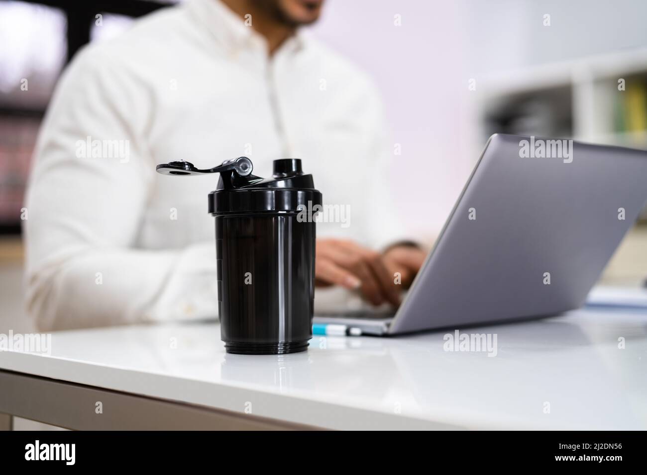 Protein Shake On Desk And Man In Foreground Using Computer Stock Photo
