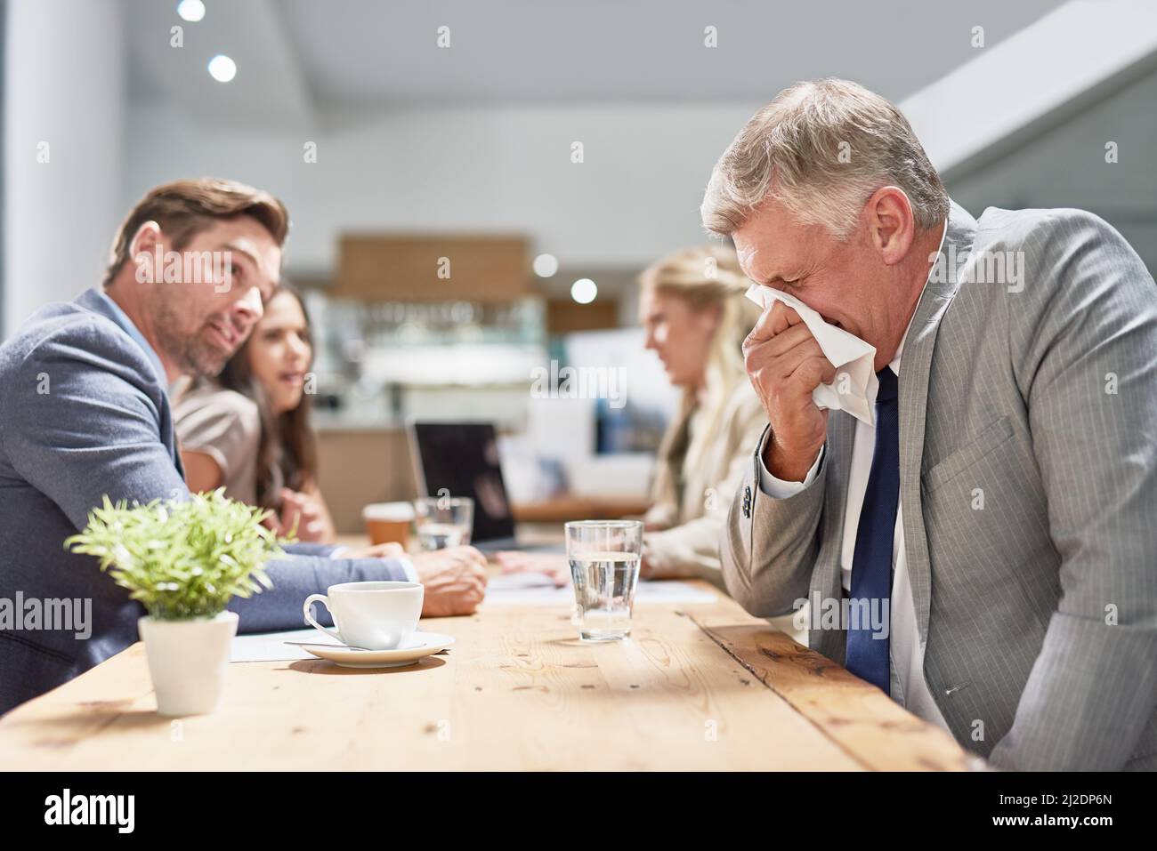 His allergies are drawing unwanted attention. Cropped shot of a businessman blowing his nose while his colleagues look on in disgust. Stock Photo