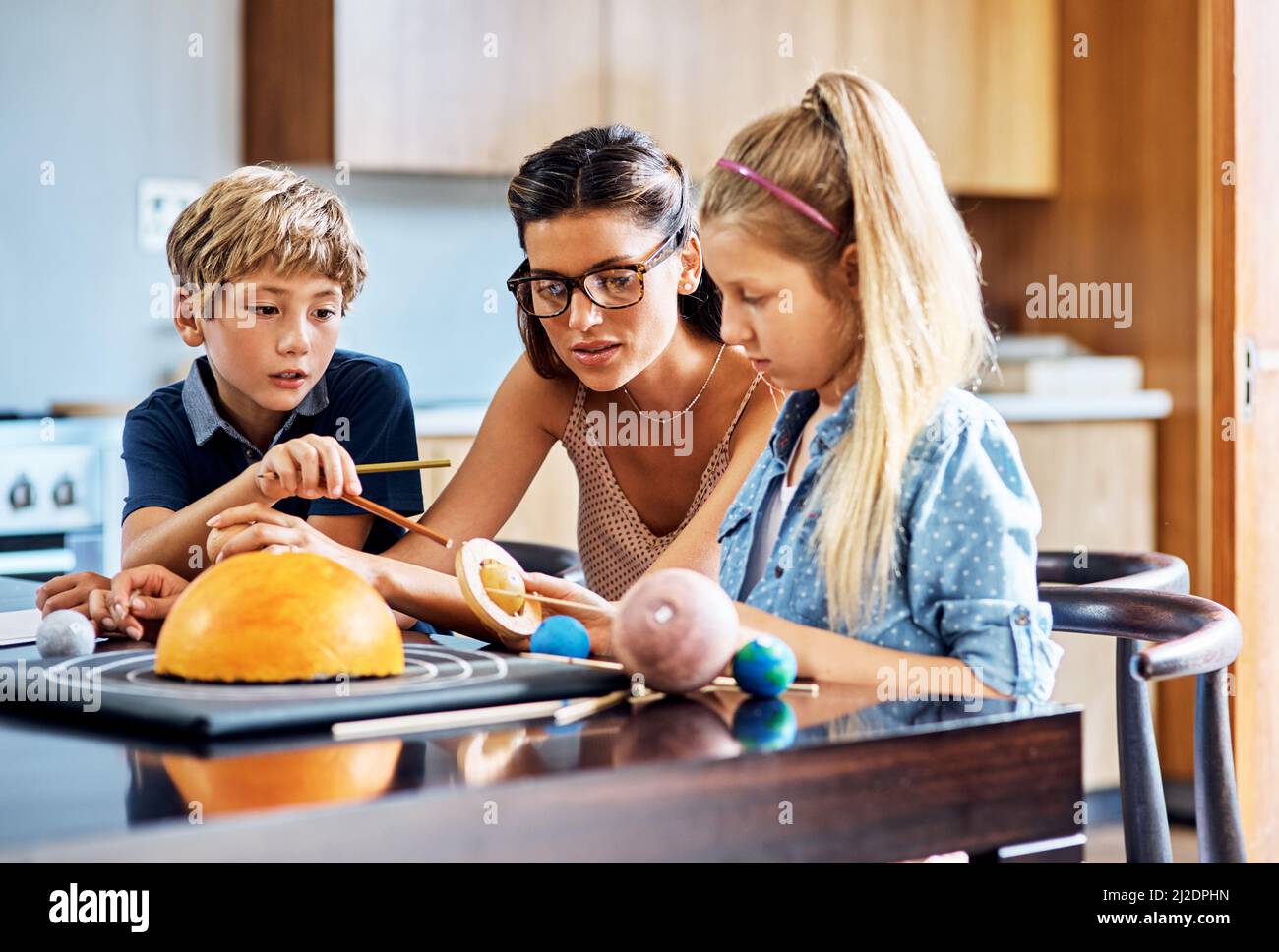 Learning all about outer space. Shot of a mother helping her two young children with a school project at home. Stock Photo