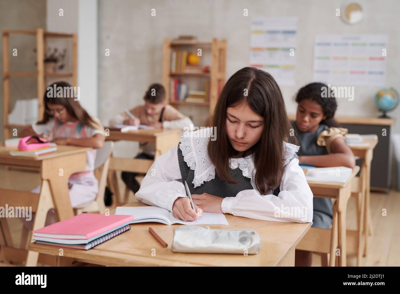 Portrait of schoolgirl wearing uniform while sitting at desk in ...