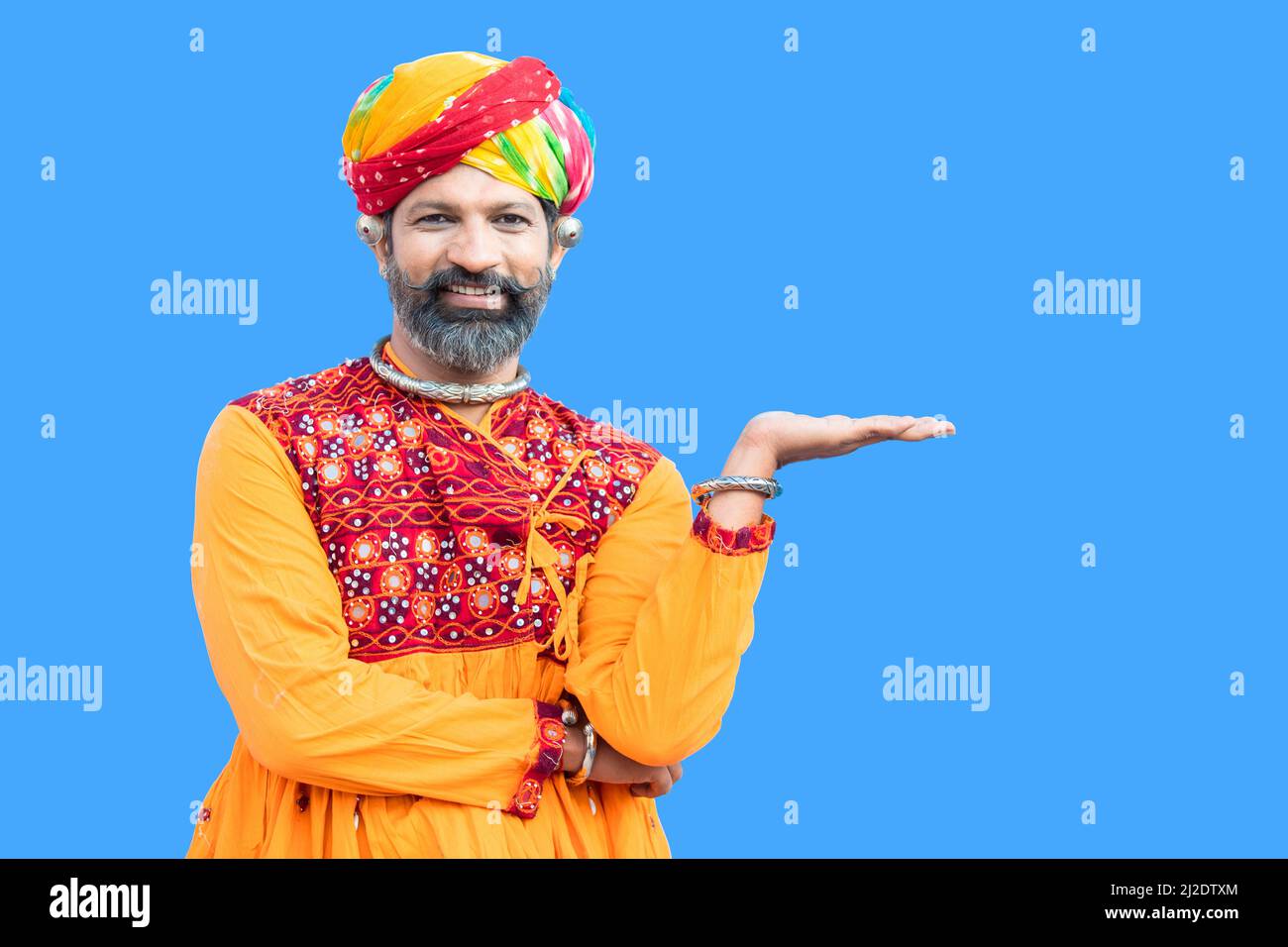 Portrait beard indian rajasthan man wearing traditional colorful outfit and turban holding palm of a hand with empty space for product or advertisemen Stock Photo
