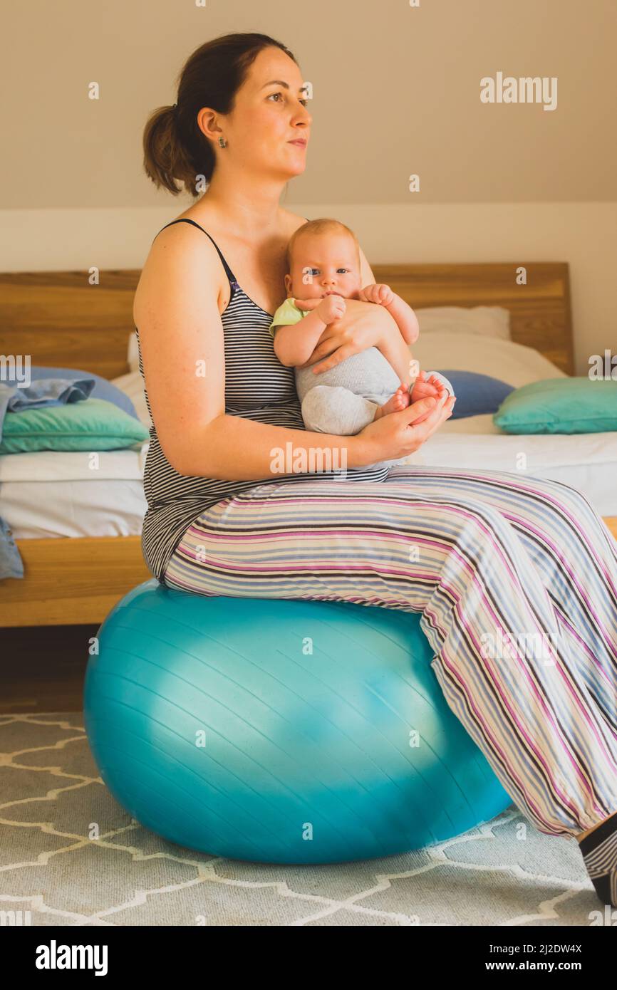Mother holding and rocking baby sitting on fitball Stock Photo - Alamy