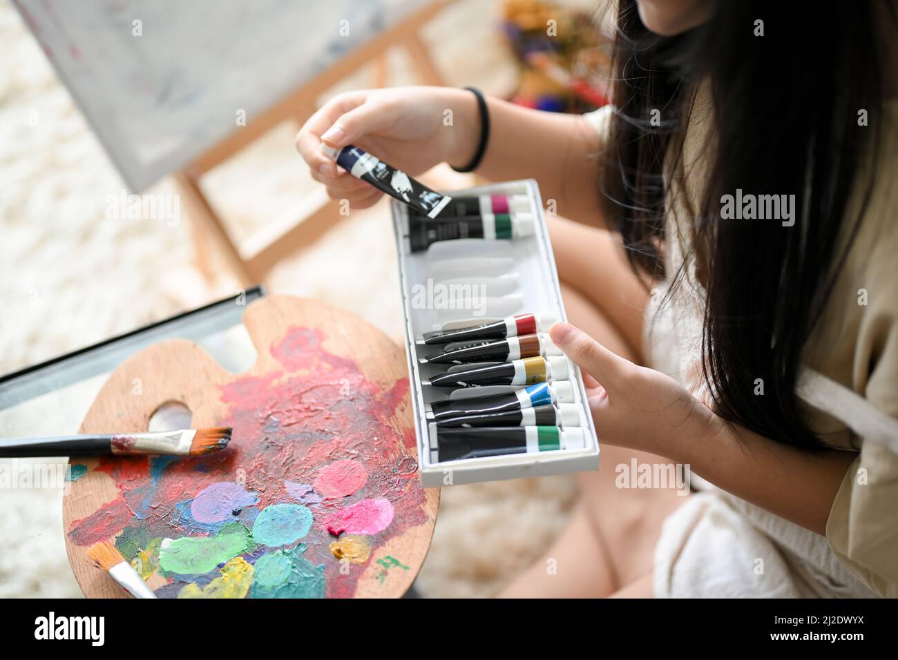 A girl enjoy colouring acrylic colours at her house, choosing a colour for her artwork. Creative activity for kids concept Stock Photo