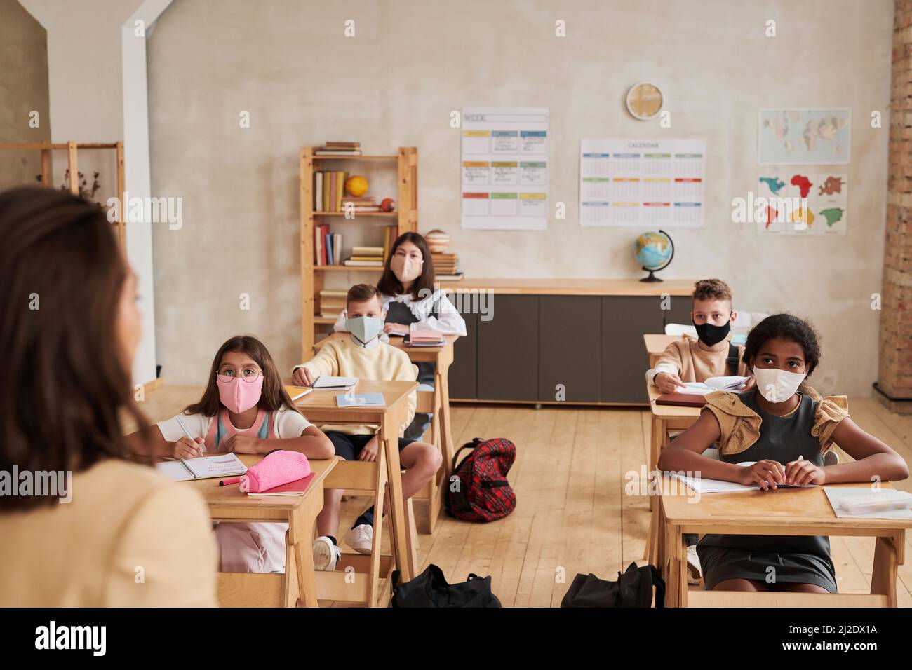 Portrait of kids wearing masks in school while sitting at desk and and looking at teacher, copy space Stock Photo