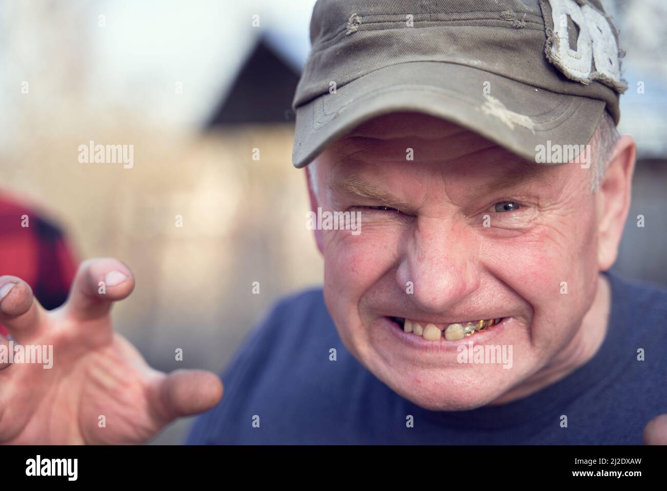 Senior man wearing old rumpled cap angry, frustrated and furious showing grin with golden teeth and raising hand palm to catch. Aggressiveness, anger and rage concept. Stock Photo