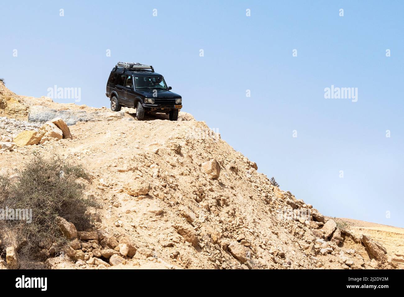 off road SUV jeep-type vehicle maneuvering down a steep descent on a barren desert mountain with a clear blue sky background Stock Photo