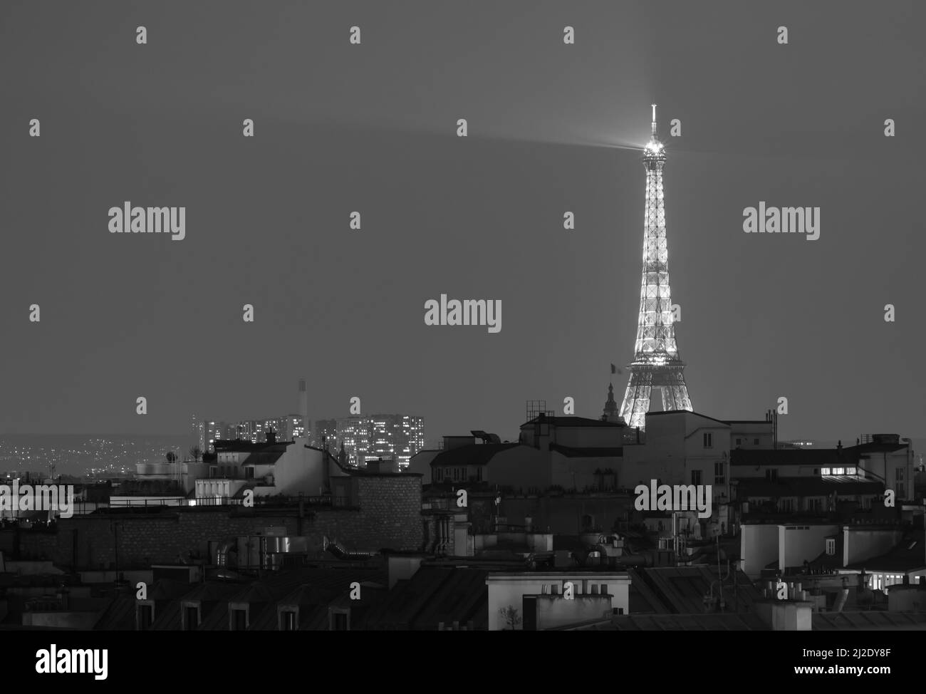 View of the stunning illuminated Eiffel Tower above the rooftops of Paris in black and white Stock Photo