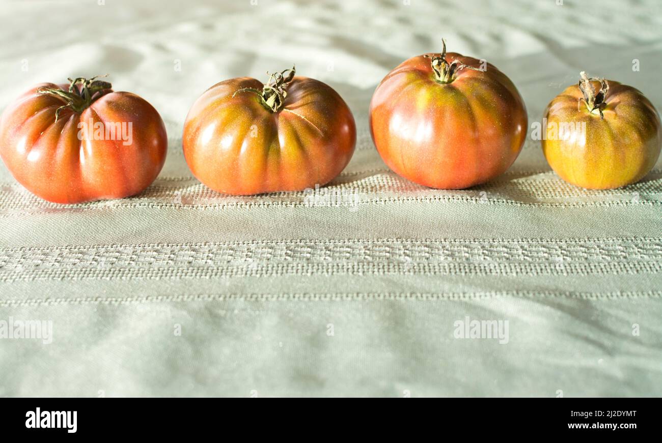 Four Black Krim heirloom tomatoes sitting on a table. Stock Photo