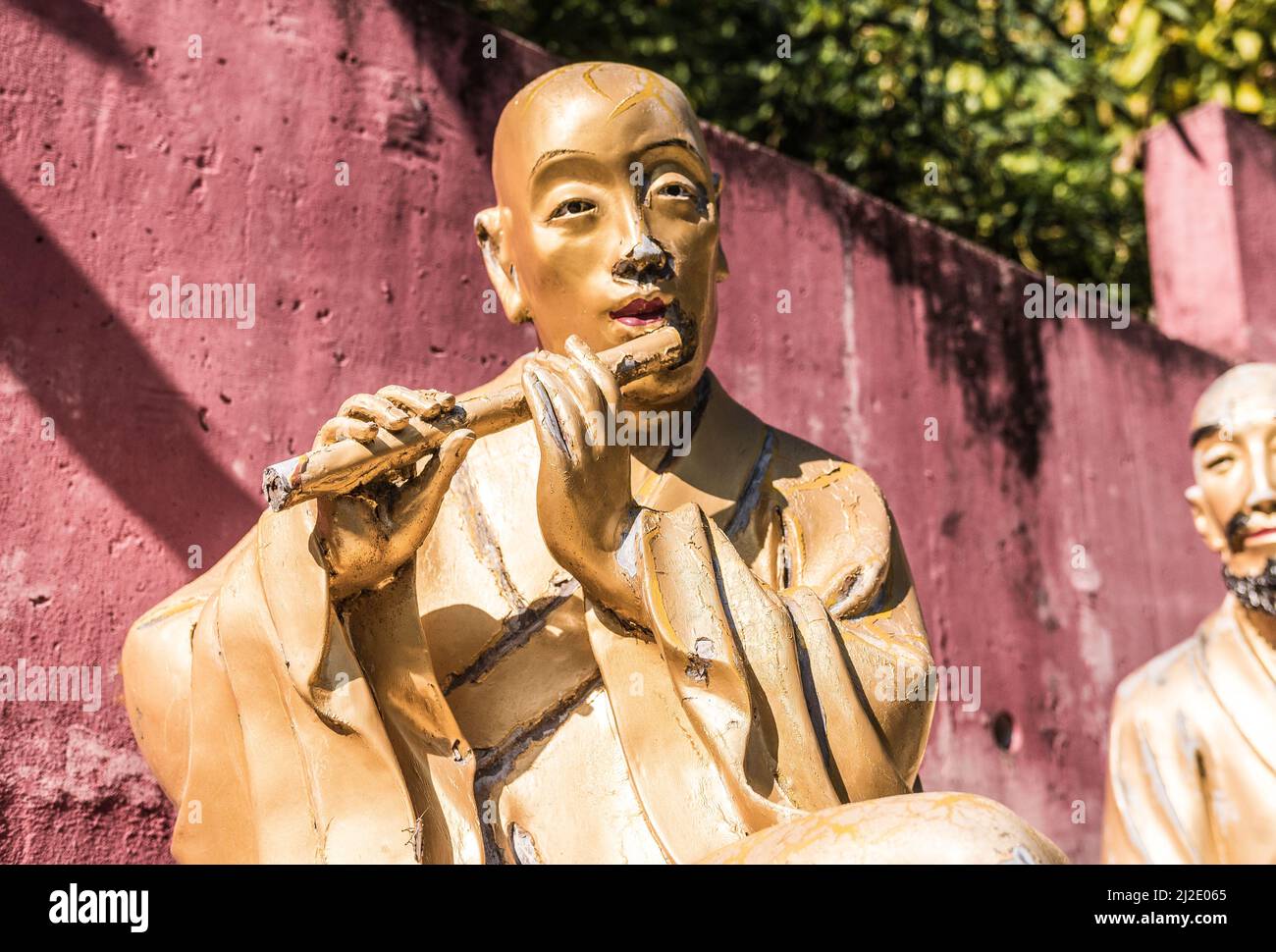 Beautiful buddha statue unique close shot. Golden sculpture representing a monk playing the flute. Ten Thousand Buddhas Monastery, Hong Kong. Stock Photo