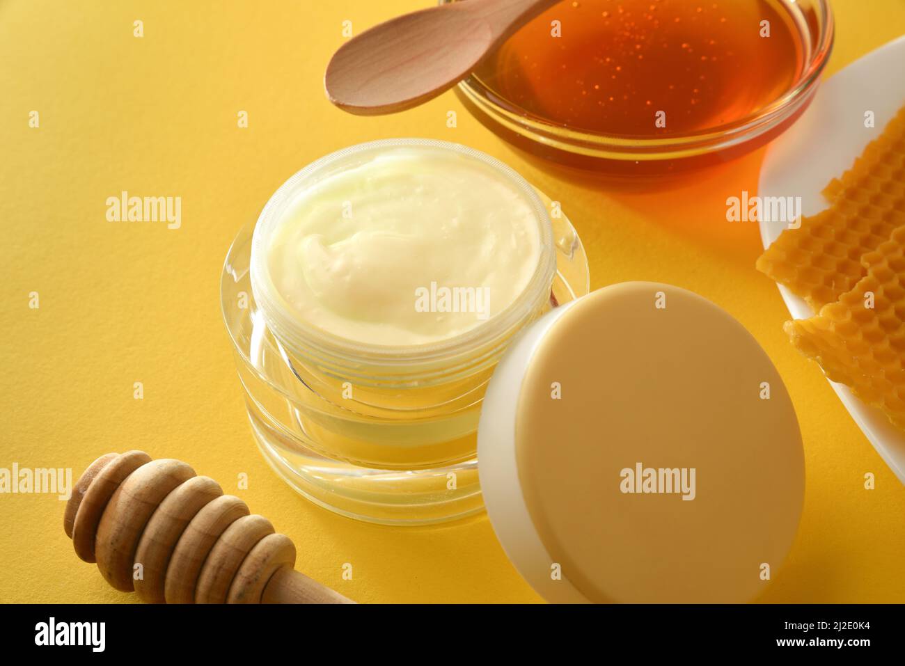 Moisturizing skin care cream with honey extracts with pot and plate with honeycombs and  pollen on yellow table close up. Horizontal composition. Elev Stock Photo