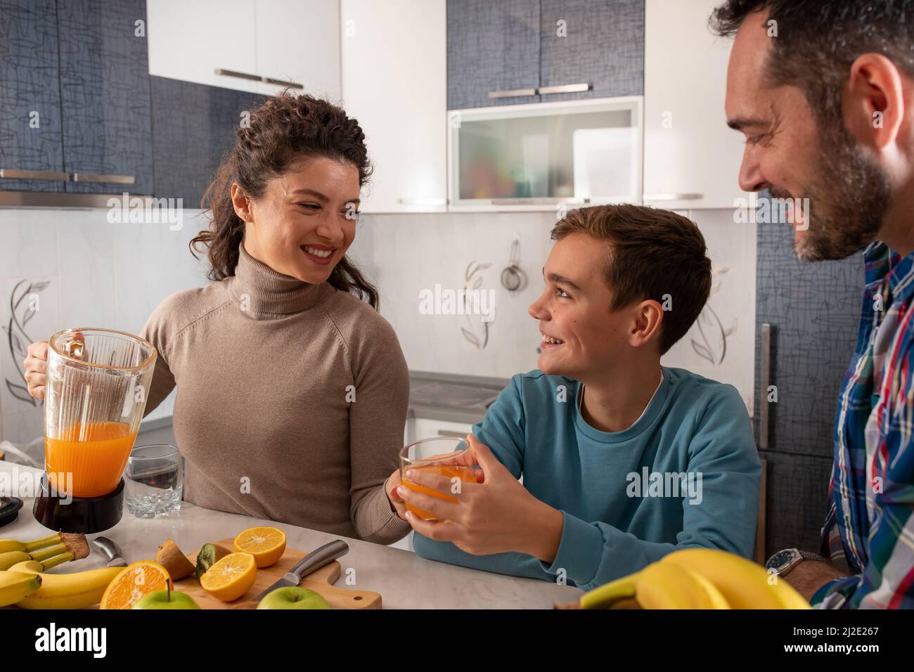 Family spends time together in the kitchen and drinks freshly squeezed orange juice. Stock Photo