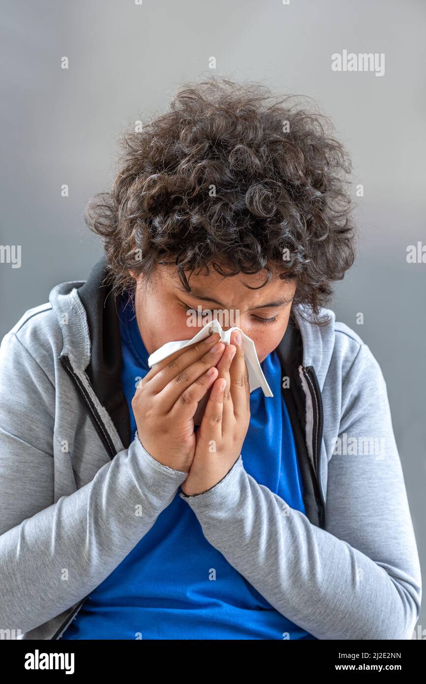 Young teenager cold flu illness tissue blowing runny nose - kid blowing his nose. seasonal virus caught Stock Photo