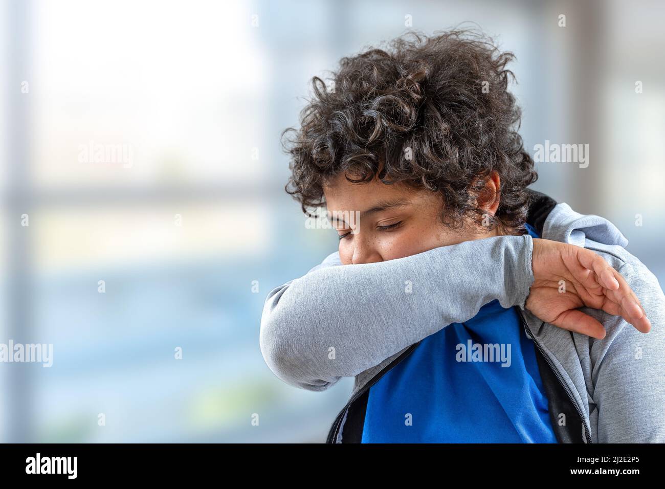 Yong boy teenager sneezing into his elbow.to avoid infecting others Stock Photo