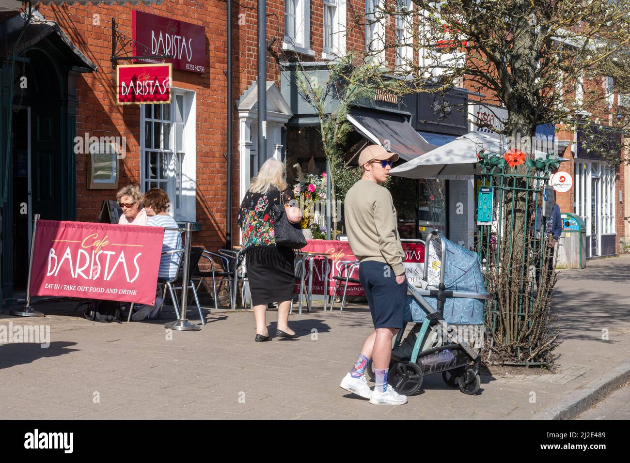 Hartley Wintney village centre, Hampshire, England, UK. View of the High Street with young man looking after a baby in a pram Stock Photo