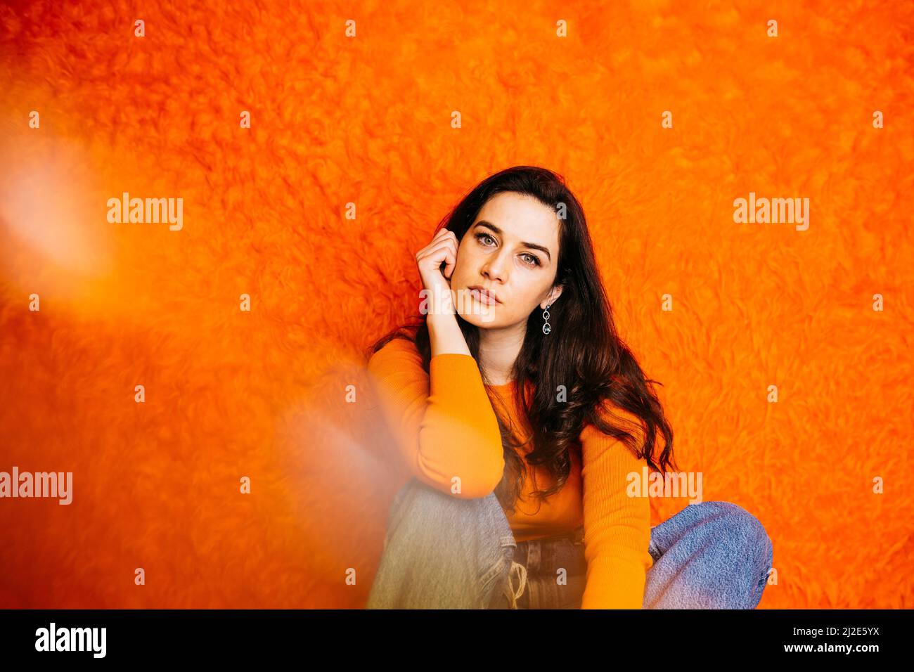 Portrait of brunette caucasian young woman with long hair, sitting against an orange haired background Stock Photo
