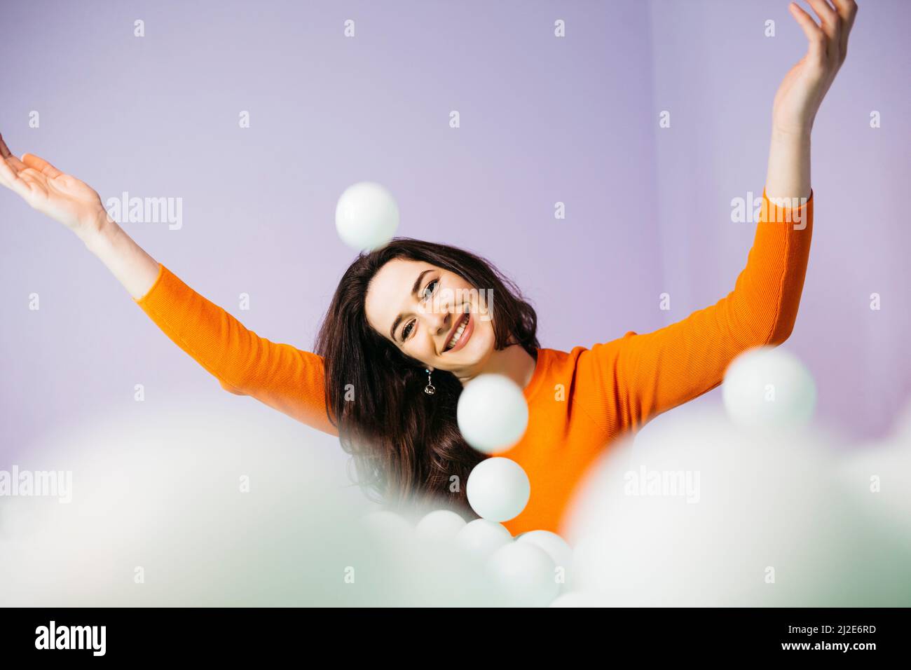 Portrait of brunette caucasian young woman with long hair, sitting in a swimming pool filled with balls and throwing them to the air Stock Photo