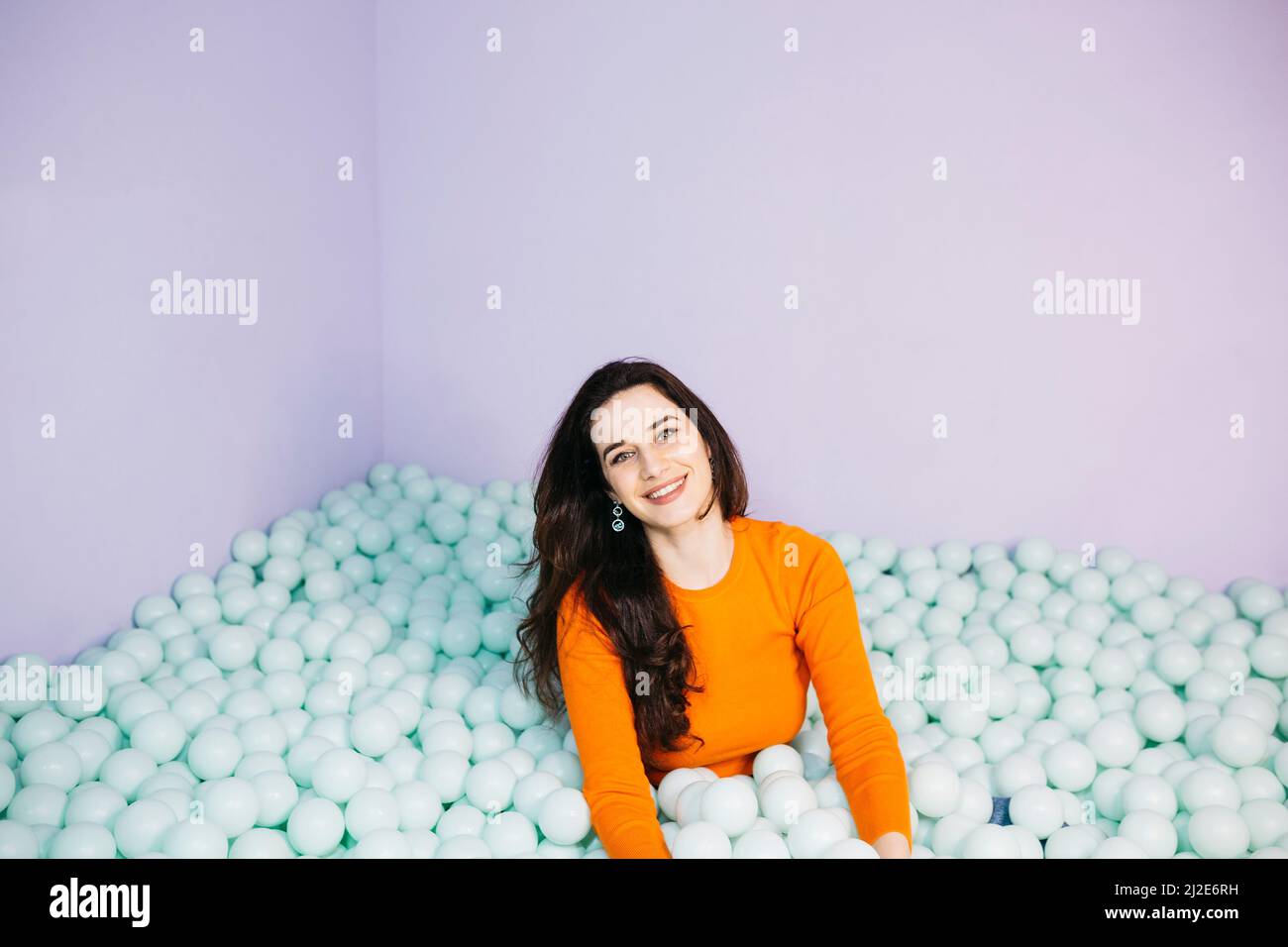 Portrait of brunette caucasian young woman with long hair, sitting in a swimming pool filled with balls Stock Photo