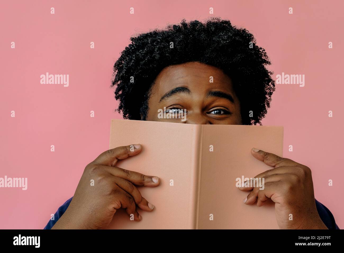 african american man posing with a book in the studio over pink background male model Stock Photo