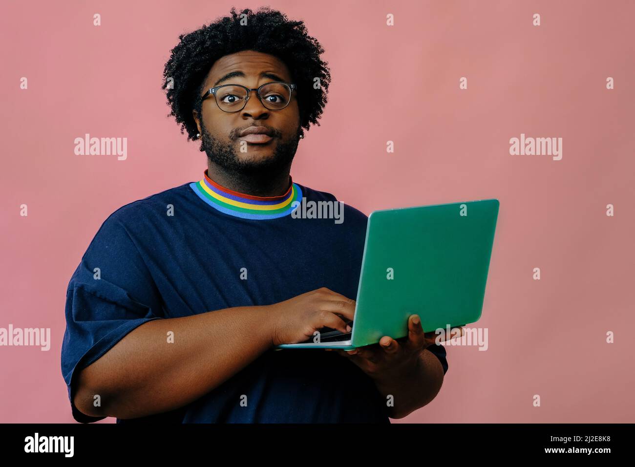 young african american man posing with laptop in the studio over pink background male model Stock Photo