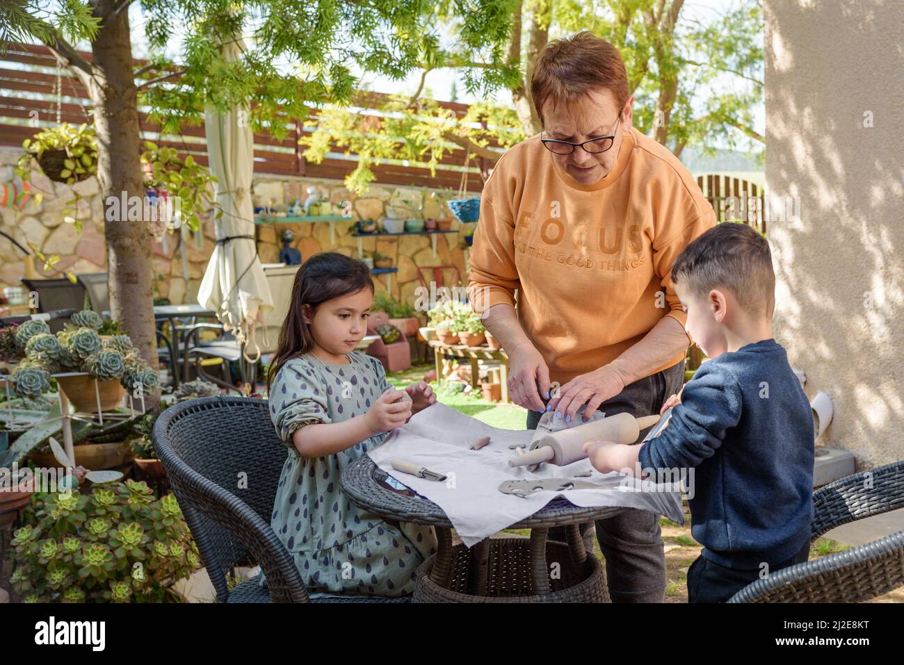 Little children with grandmother modeling with black clay on a table in garden. Stock Photo