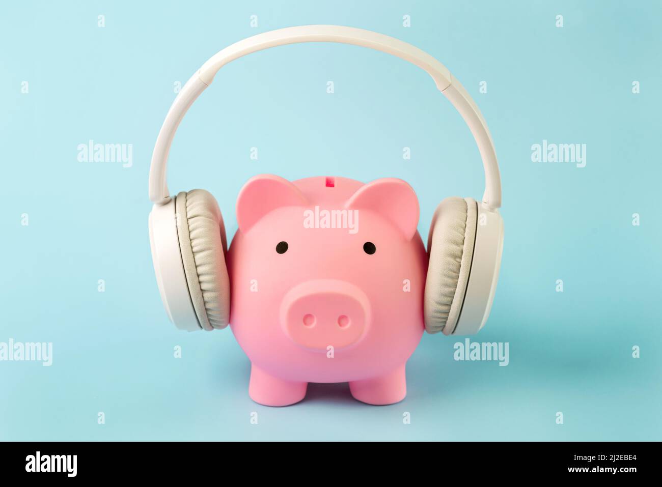 Pink piggy money bank with white wireless headphones over blue background Stock Photo