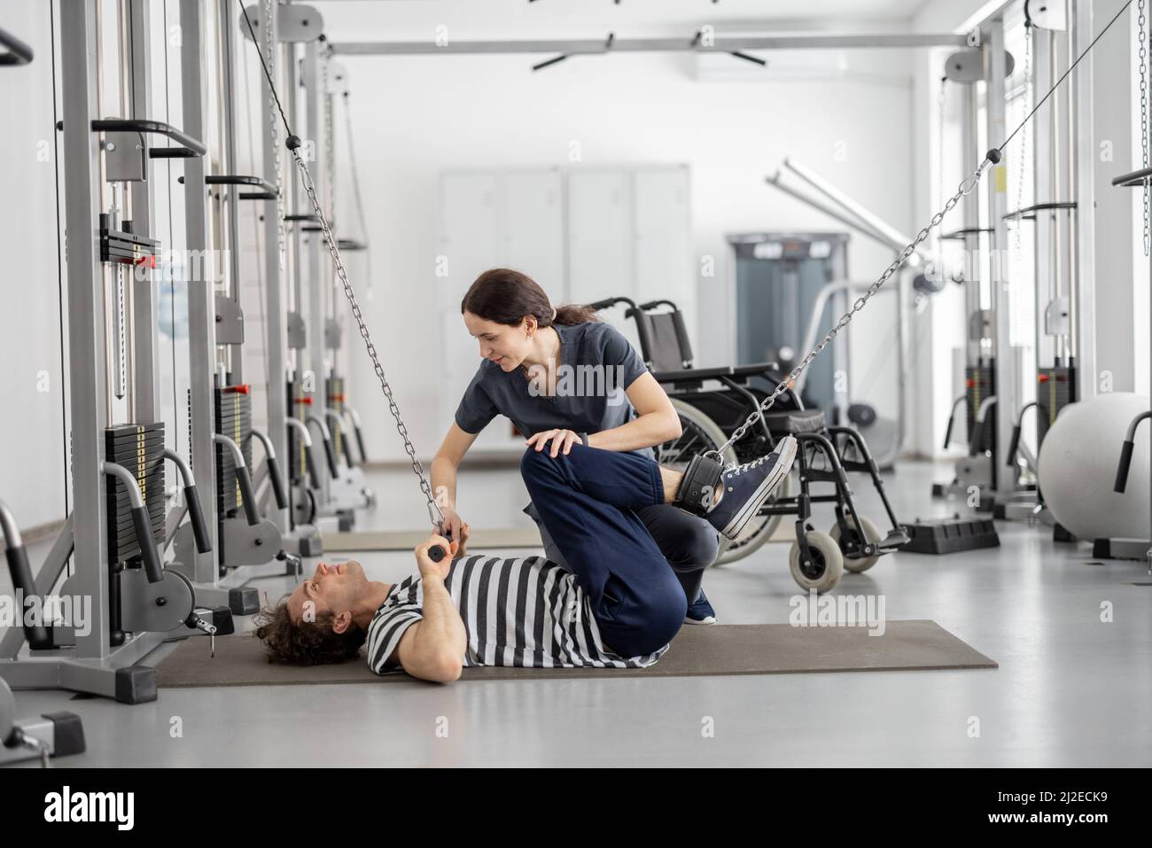 Rehabilitation specialist helps a guy to do exercise on decompression simulator for recovery Stock Photo