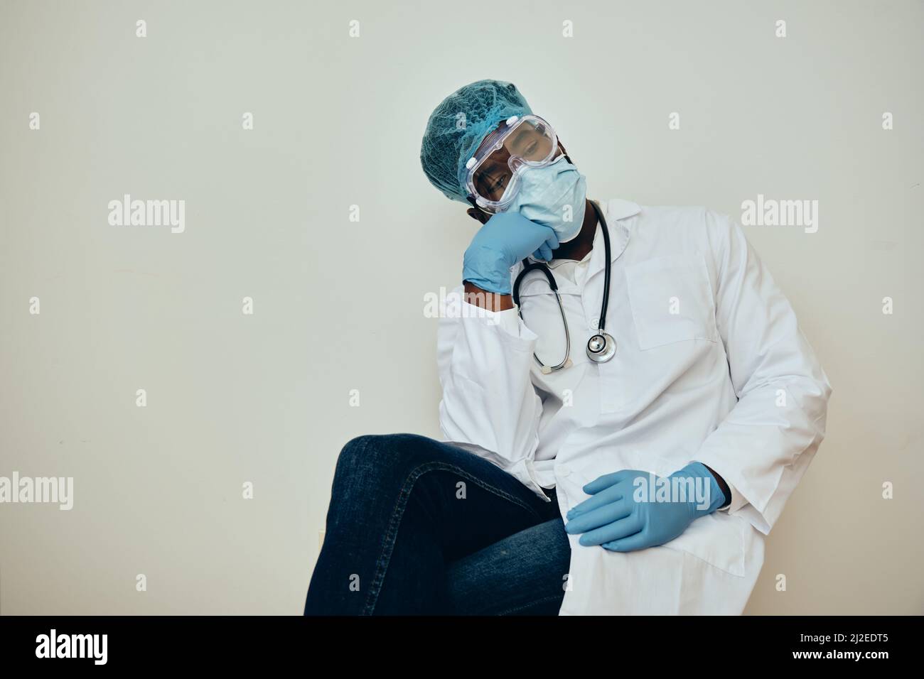 Exhausted male healthcare worker sitting on chair against white wall at