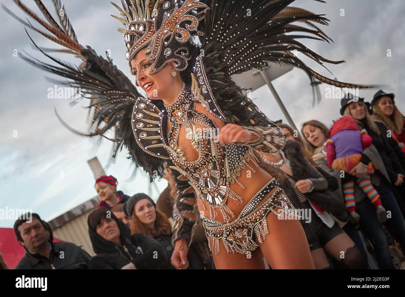 Portugal Carnaval, Mealhada - Woman in black and gold  feathered costume dancing samba with Bate no Tambor. Stock Photo