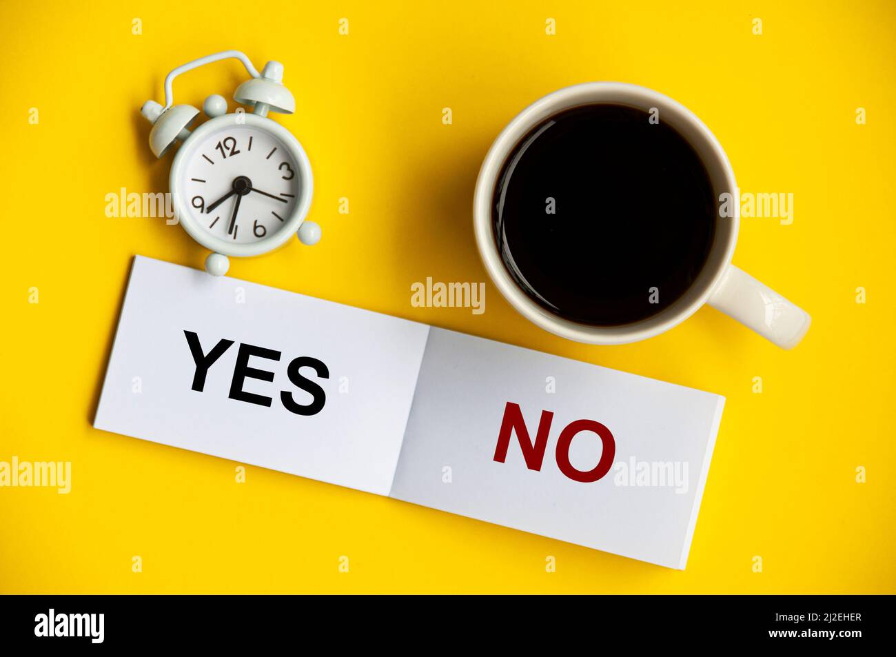 Yes and no text on notepad with alarm clock and coffee cup on yellow background. Decision making concept. Stock Photo