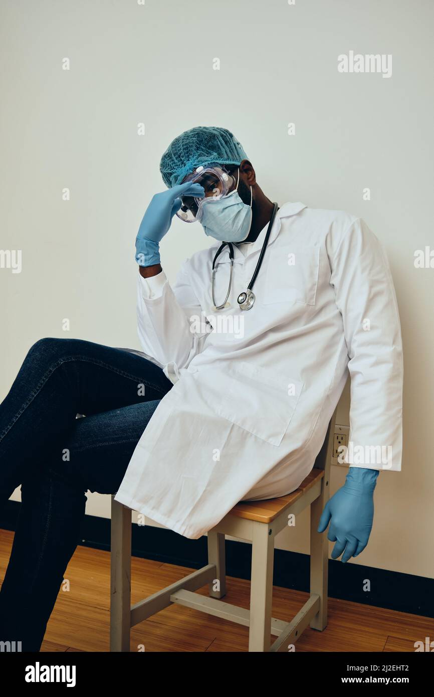 Exhausted male healthcare worker sitting on chair against white wall at