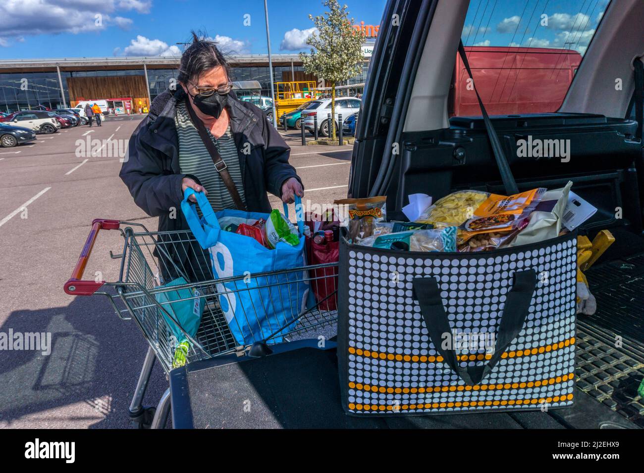 Woman unloading her weekly shop from trolley in a supermarket car park into the back of her car.  NB: Model release available for person in foreground Stock Photo