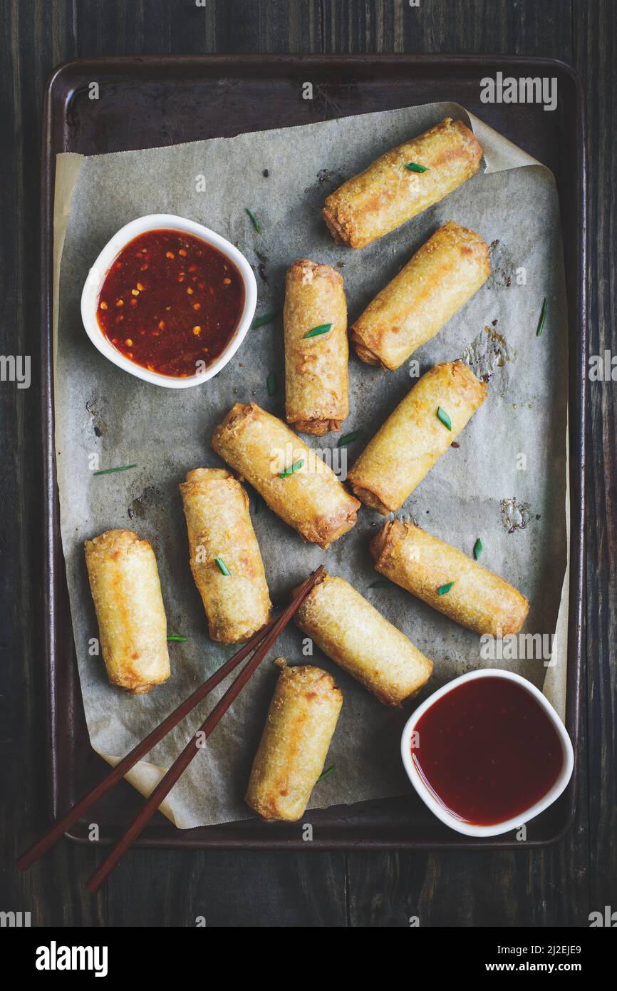 Top view of egg rolls in sweet and sour sauce over a dark rustic table with chop sticks. Garnished with green onions. Overhead table top view. Stock Photo