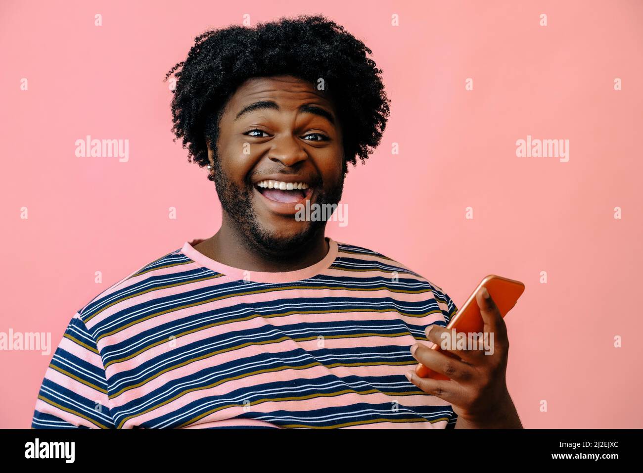 young happy black man with smart phone in the studio over pink background male model Stock Photo