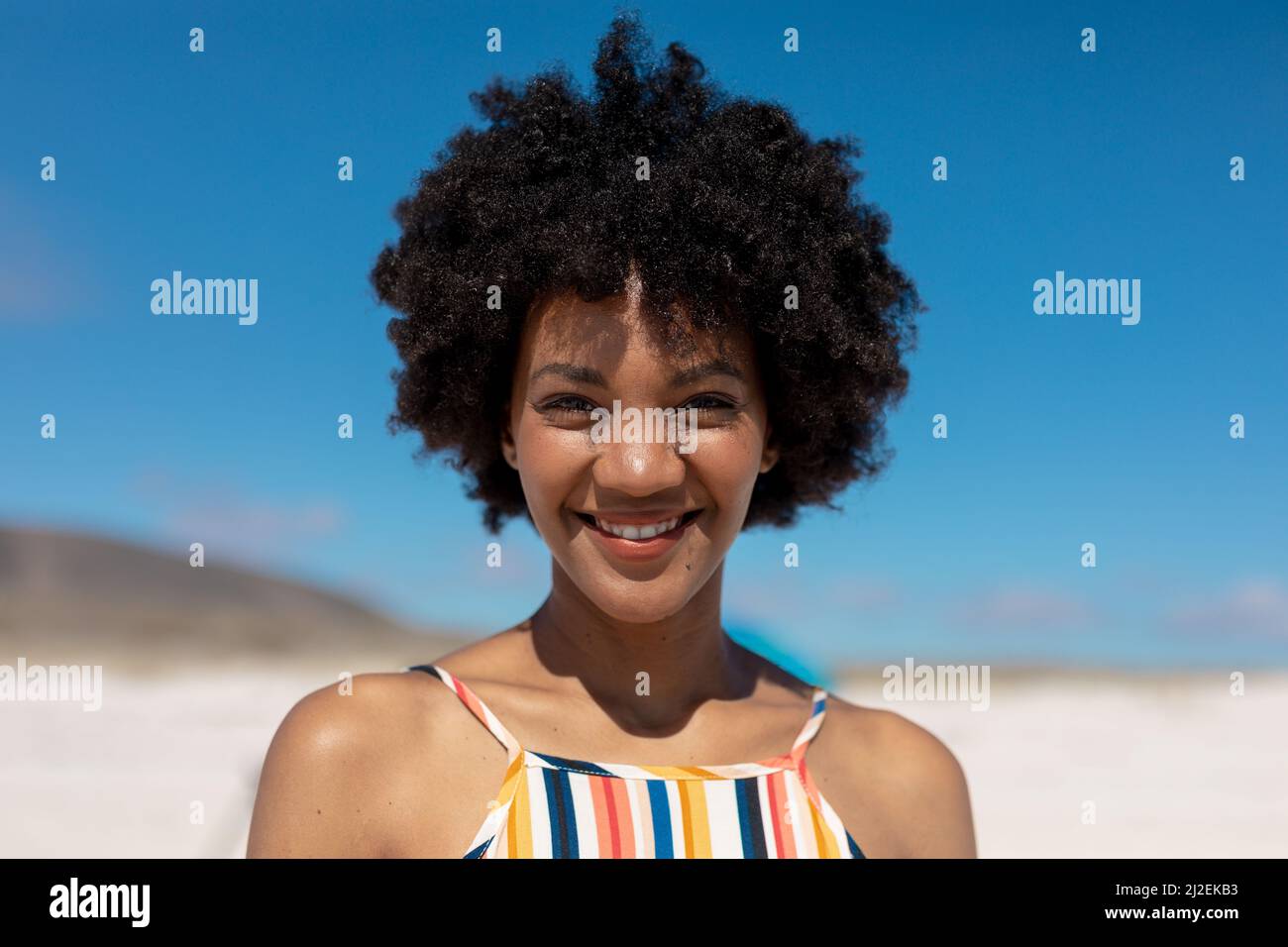 Portrait of smiling african american woman with black afro hair at beach on sunny day Stock Photo