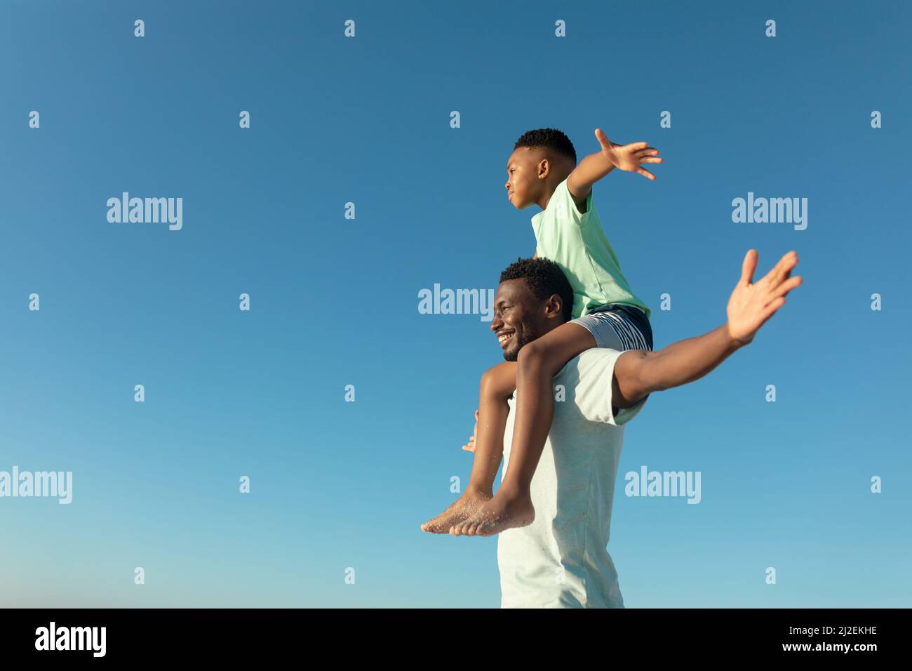 Happy african american boy on father's shoulders by copy space against clear blue sky Stock Photo
