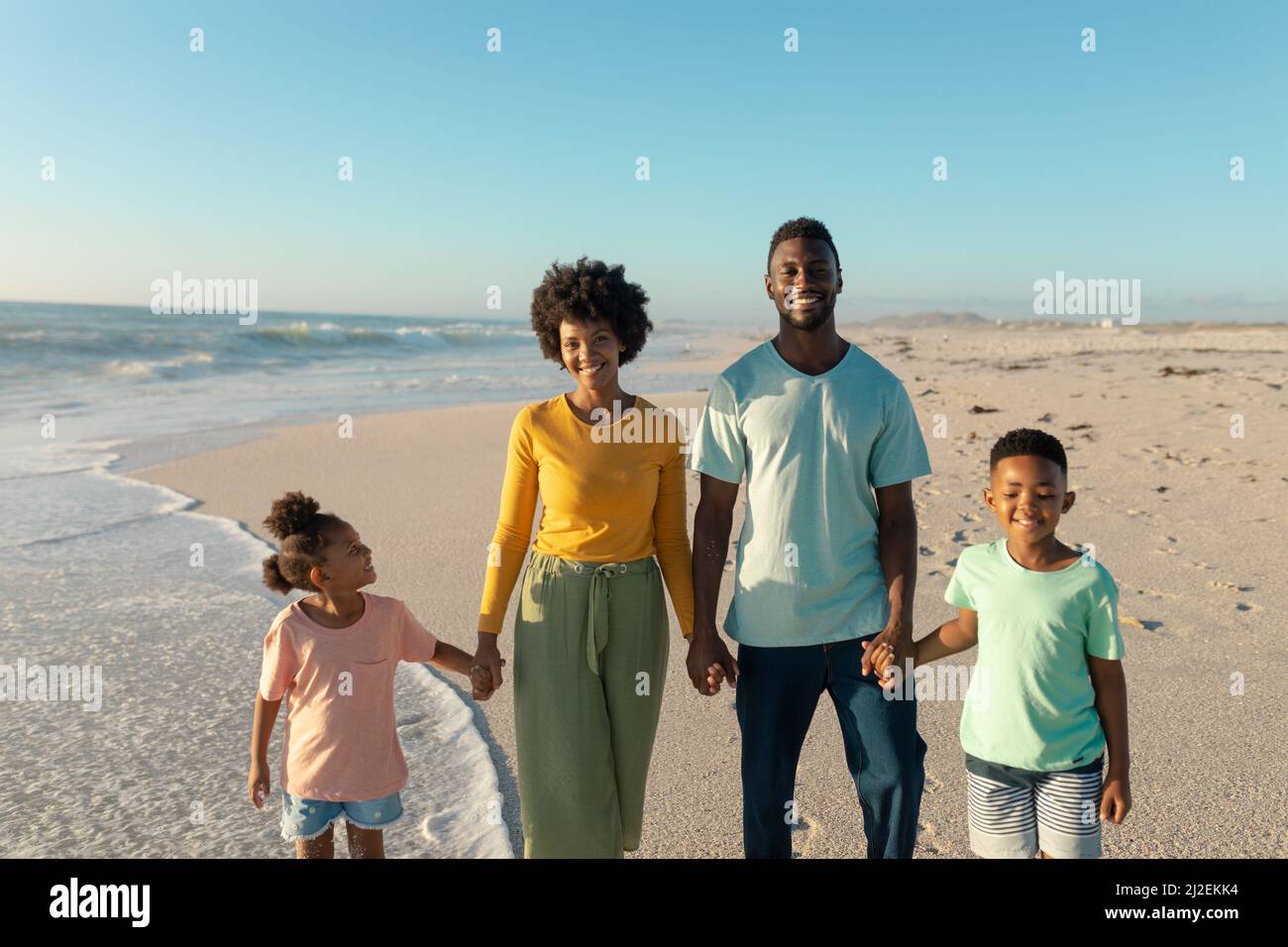Portrait of happy african american family holding hands while standing at beach against blue sky Stock Photo