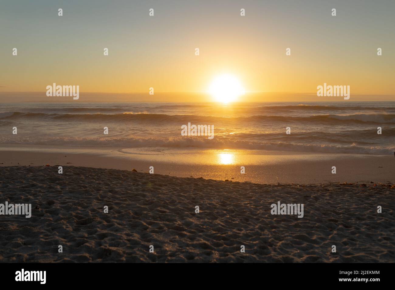 Idyllic shot of orange sun setting over sea seen from beach Stock Photo