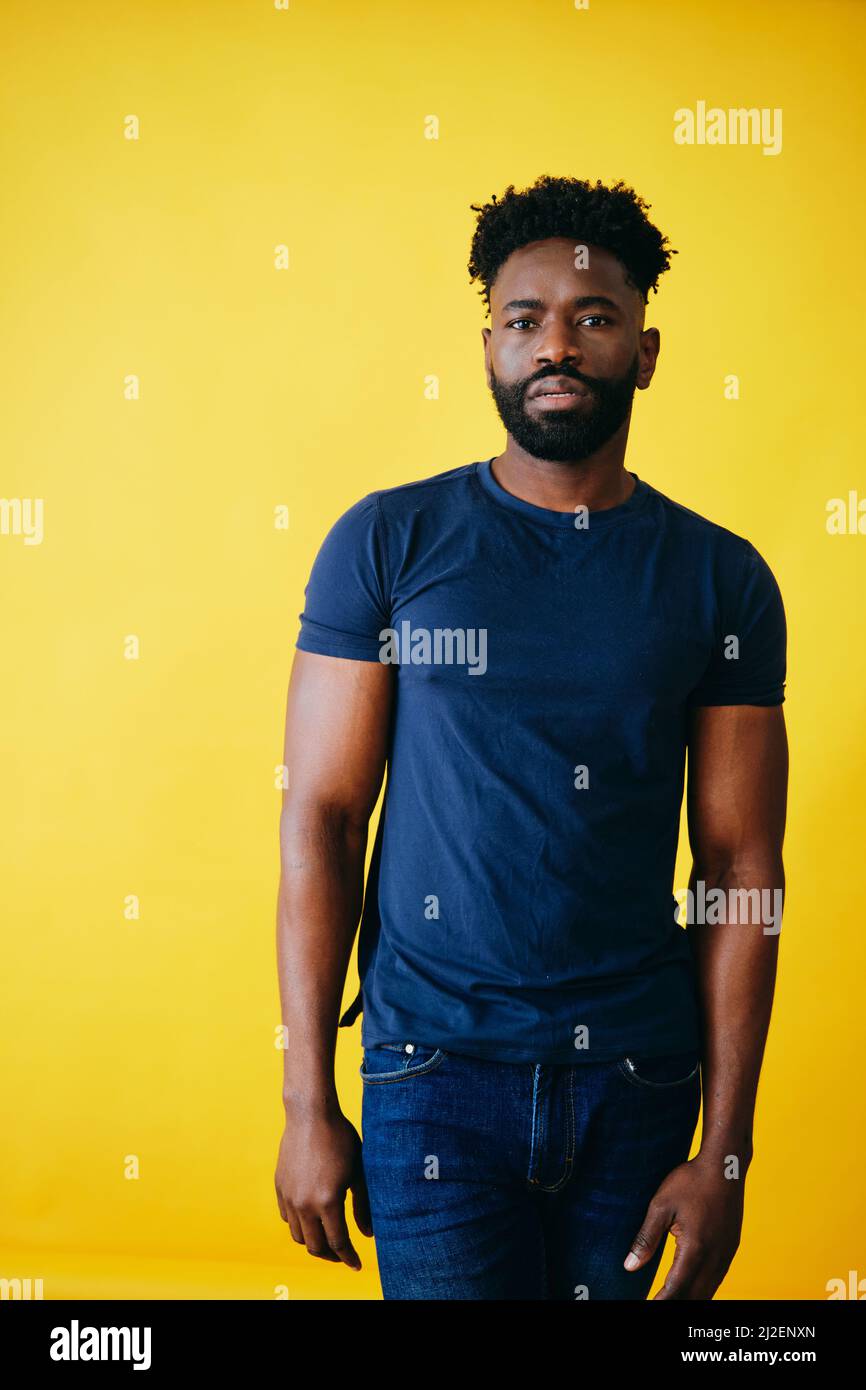 Handsome bearded man with muscular build standing against yellow background Stock Photo