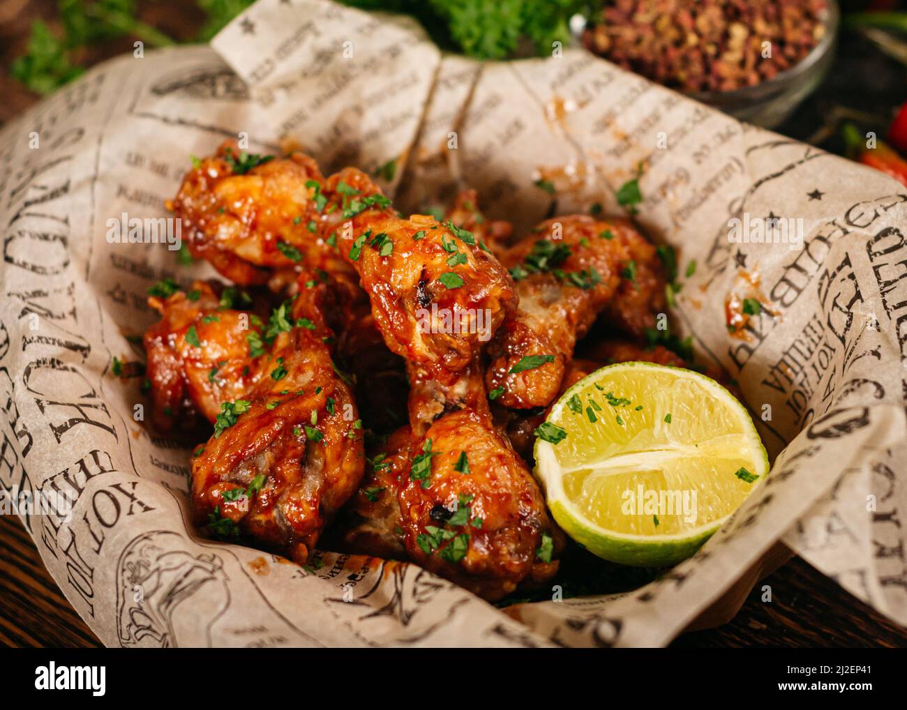 Portion of chicken drumsticks deep fried and in covered in (seasoned with) hot sauce. Served with a half of lime on craft paper. Stock Photo