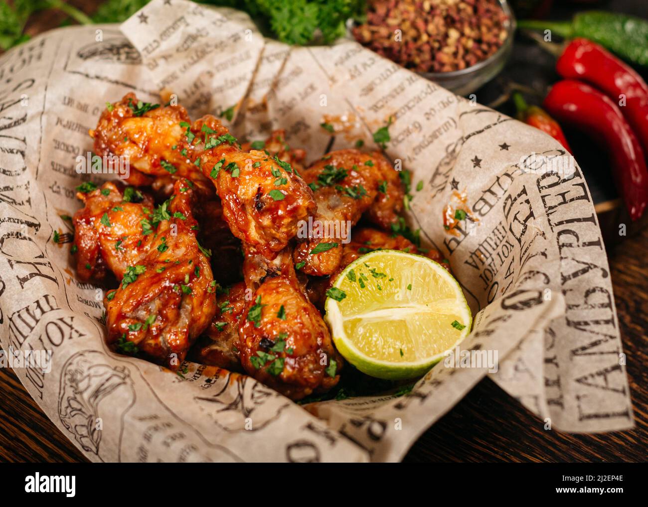 Portion of chicken drumsticks deep fried and in covered in (seasoned with) hot sauce. Served with a half of lime on craft paper. Stock Photo
