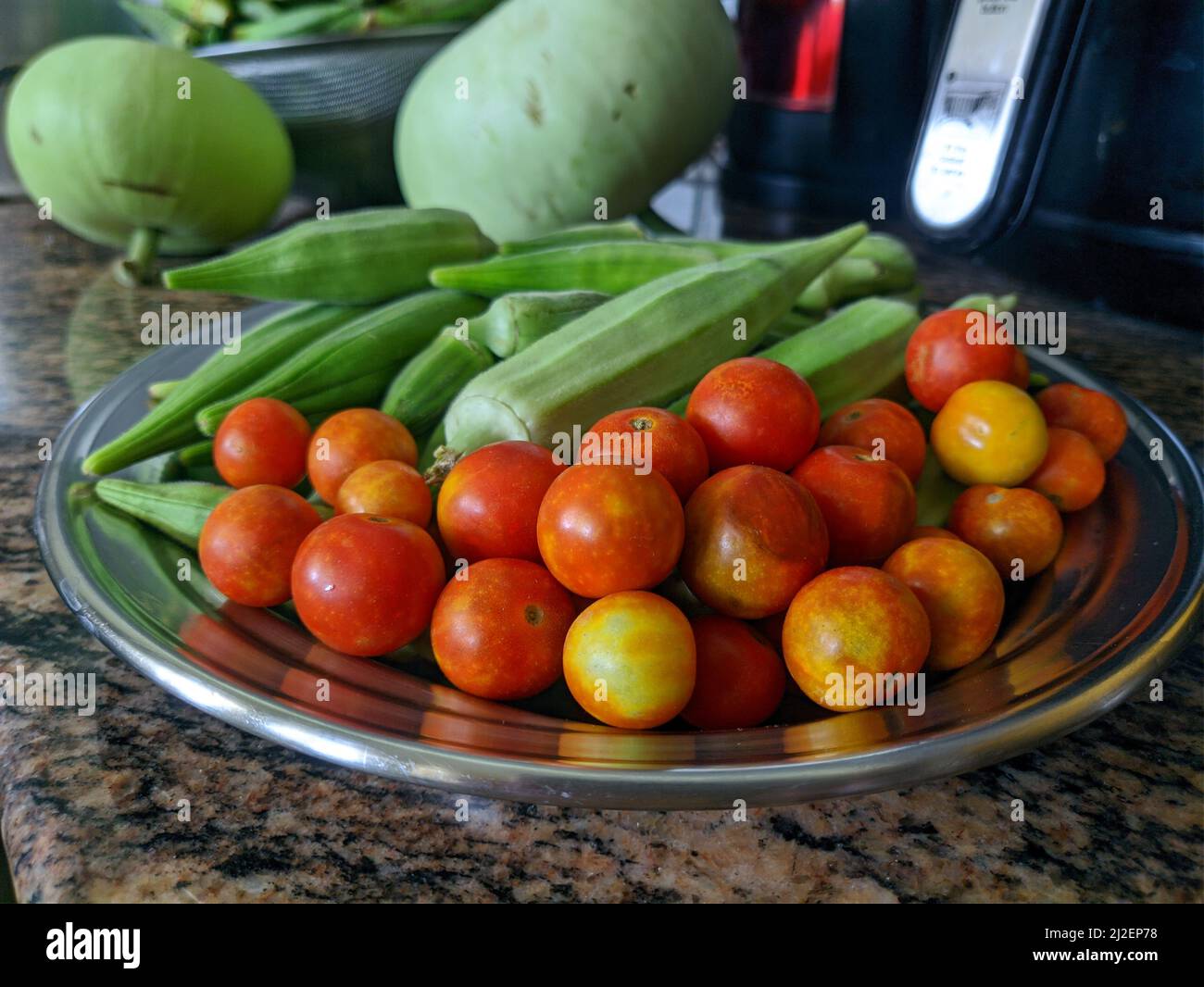 A photo of okra and cherry tomatoes in a stainless steel plate on a