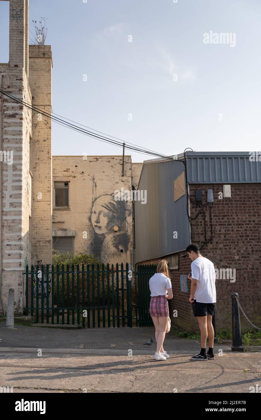 Two people visit Banksy's The Girl with a Pearl Earring graffiti work near the marina in Bristol, UK. Stock Photo