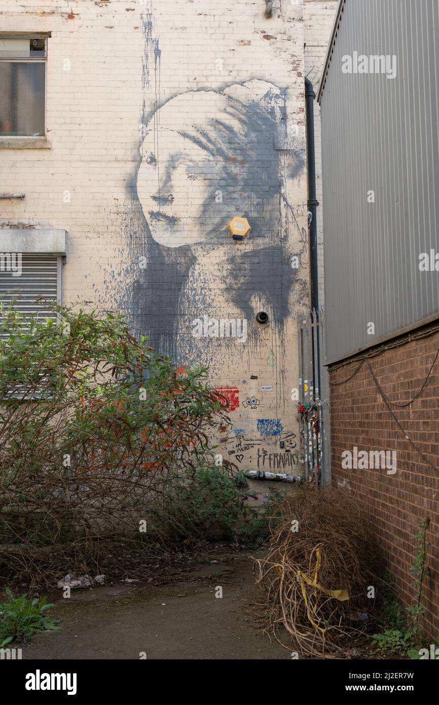 Banksy's The Girl with a Pearl Earring graffiti work near the marina in Bristol, UK, taken through the fence. Stock Photo